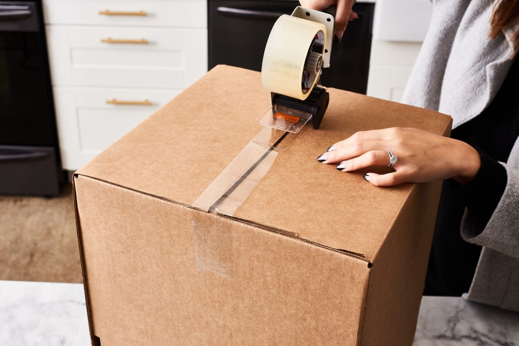 a woman sealing a cardboard box with packing tape