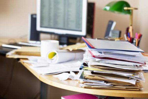 A messy office desk with a tall pile of papers