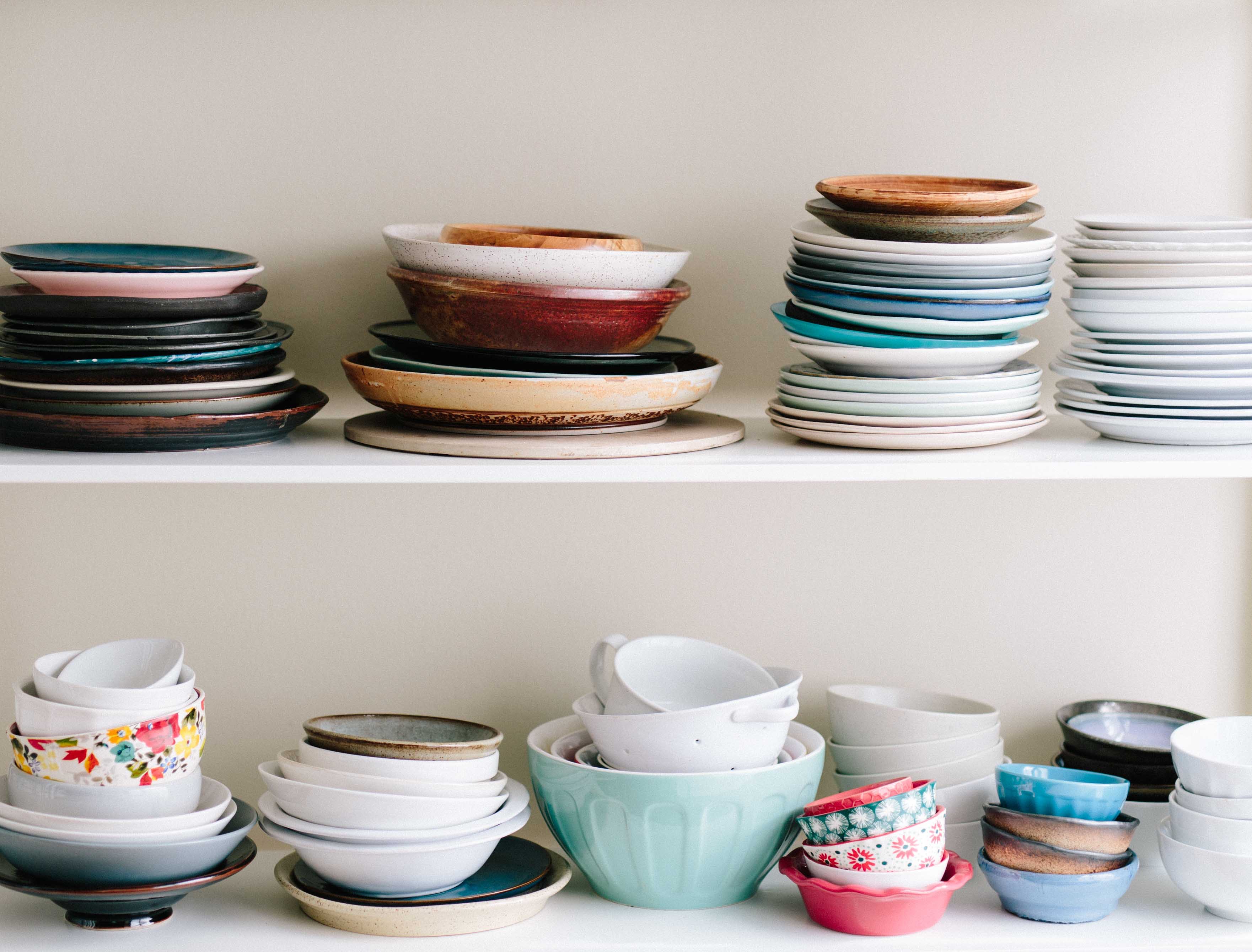 bowls and plates stacked on top of each other on 2 white shelves